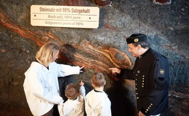 Bergwerksführer zeigt einer Familie eine Steinsalzader im Salzbergwerk