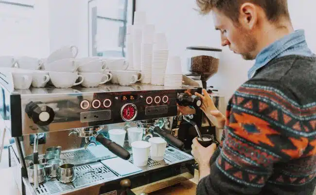 Barista arbeitet an einer professionellen Espressomaschine und schäumt Milch für ein Kaffeegetränk.