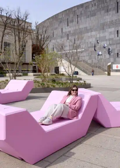 Person sitzt auf rosa Enzi im MuseumsQuartier Wien vor moderner Museumsarchitektur