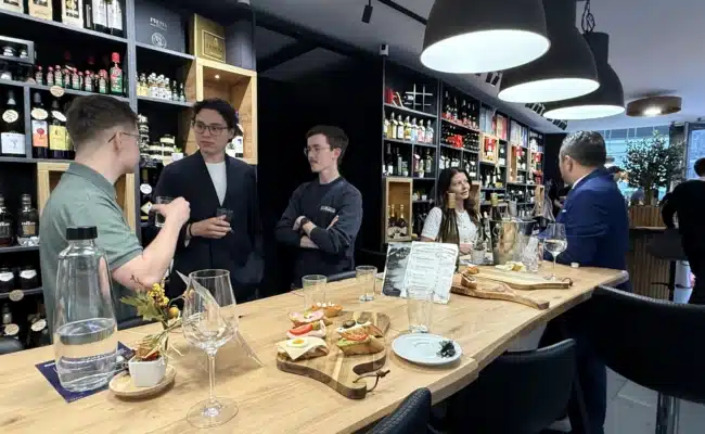Gäste im Wiedner Wein Eck beim gemeinsamen Austausch zwischen Weinregalen und Verkostungsbereich.