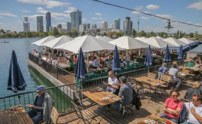 Gäste auf der Wasserterrasse des Strandcafés mit Blick auf die Wiener Skyline