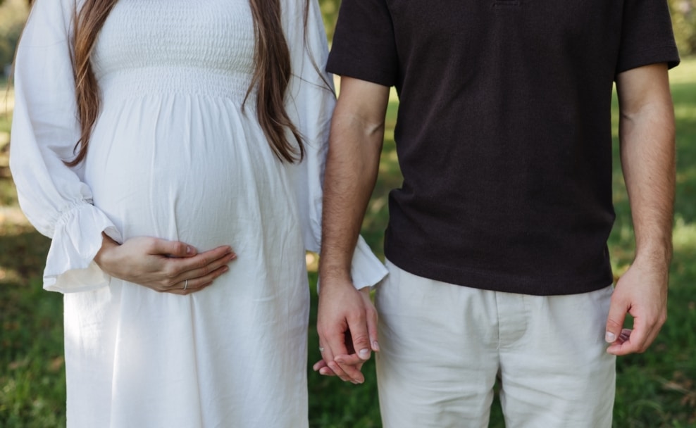 chwangere Frau und Partner halten im Freien Händchen – Symbolbild für Kinderwunsch, Familie und Geburtenrate in Österreich