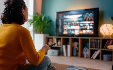 Frau nutzt Smart-TV mit Streamingplattform und moderner Addressable-TV-Werbung im Wohnzimmer