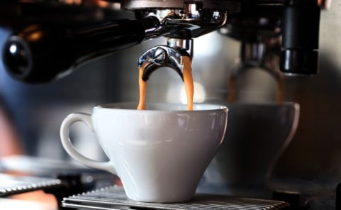 Frisch gebrühter Espresso fließt aus einem Siebträger in eine Espressotasse.