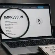 Laptop mit geöffneter Impressumsseite und Lupe als Symbol für Medienstandards, Transparenz und Aufnahmekriterien der Digitalen Allianz.