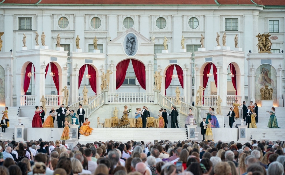 Zuschauer verfolgen eine Open-Air-Opernaufführung des Wiener Opernsommers vor einer Bühnenkulisse in Wien.