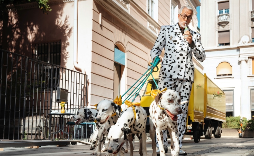Mann im Dalmatiner-Anzug führt mehrere Dalmatiner für die Kampagne „Make it extra“ von Schweppes