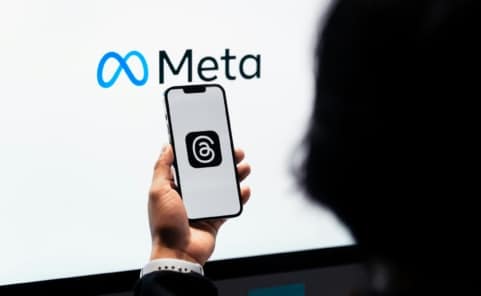 Smartphone mit Threads-App vor einem Bildschirm mit Meta-Logo als Symbolbild für den Meta-Konzern und seine Plattformen.