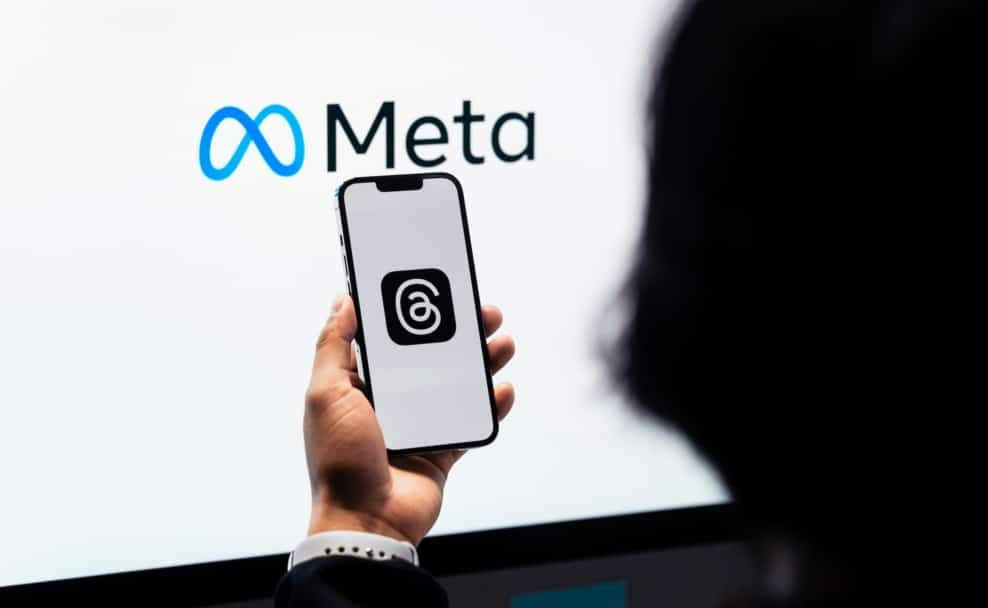 Smartphone mit Threads-App vor einem Bildschirm mit Meta-Logo als Symbolbild für den Meta-Konzern und seine Plattformen.
