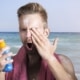 Mann trägt am Strand bei Sonne Sonnencreme auf und schützt seine Haut vor UV-Strahlung