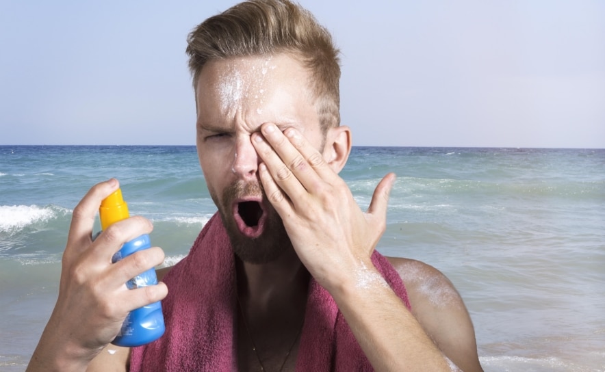 Mann trägt am Strand bei Sonne Sonnencreme auf und schützt seine Haut vor UV-Strahlung