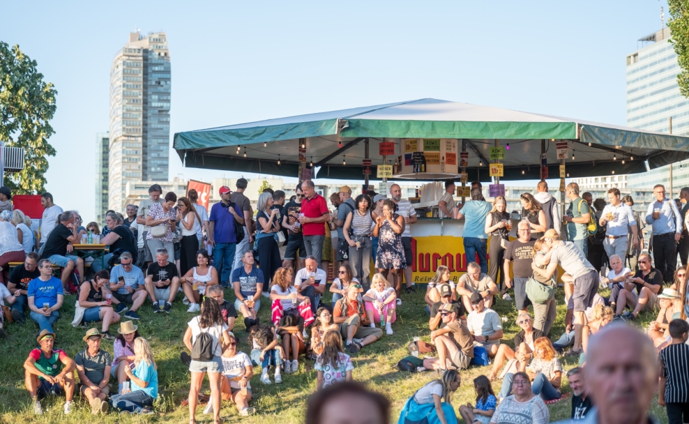 Besucher des Donauinselfests 2026 vor einem Gastronomiestand und auf der Wiese.