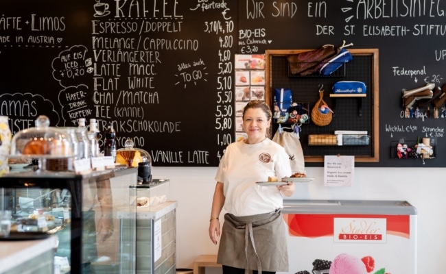 Mitarbeiterin im Mamas Café am Stephansplatz in Wien vor der Kaffeekarte und Kuchentheke
