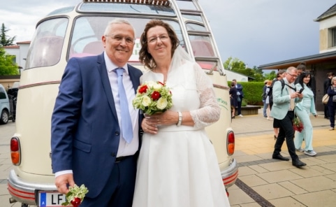 Ein Brautpaar aus „Liebesg’schichten und Heiratssachen“ vor einem Oldtimer-Bus.
