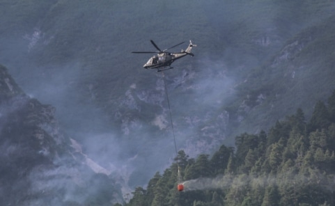 Ein AW169 Lion des Bundesheeres transportiert einen Löschwasserbehälter über bewaldetem Berggelände.