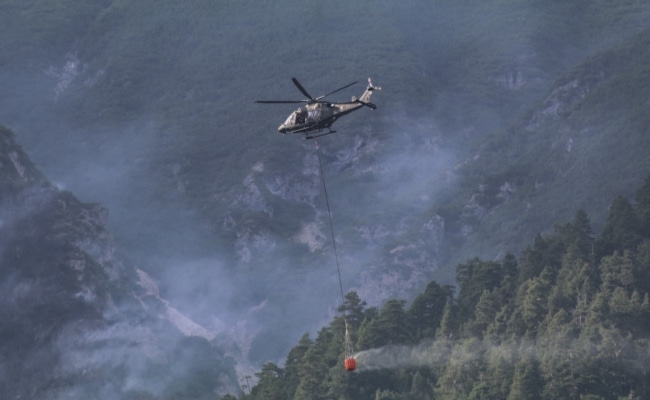 Ein AW169 Lion des Bundesheeres transportiert einen Löschwasserbehälter über bewaldetem Berggelände.
