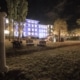 Menschen sitzen und stehen abends im Garten des beleuchteten Otto-Wagner-Areals