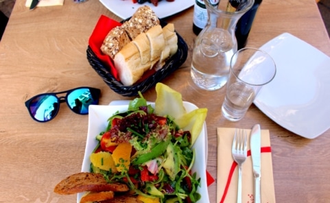 Gedeckter Restauranttisch mit Wasserkaraffe, Glas Wasser, Salat und Brotkorb