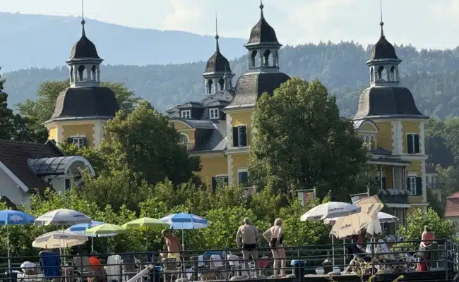 Falkensteiner Schlosshotel Velden mit sommerlich besuchter Terrasse am Strandcorso