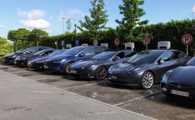 Mehrere Tesla-Fahrzeuge stehen nebeneinander an einer Reihe von Superchargern
