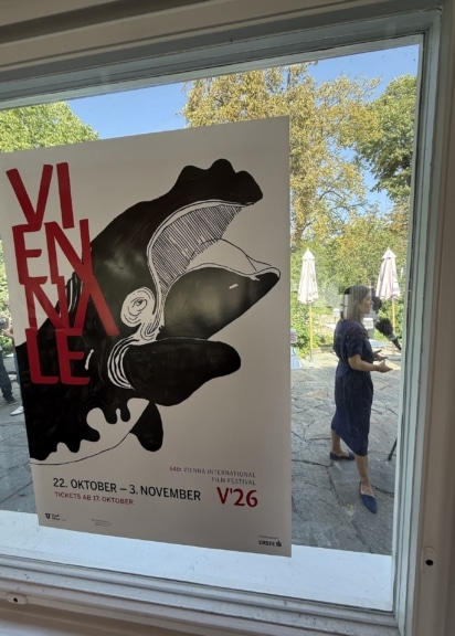 Wal-Plakat der Viennale 2026 an einem Fenster, dahinter Festivaldirektorin Eva Sangiorgi