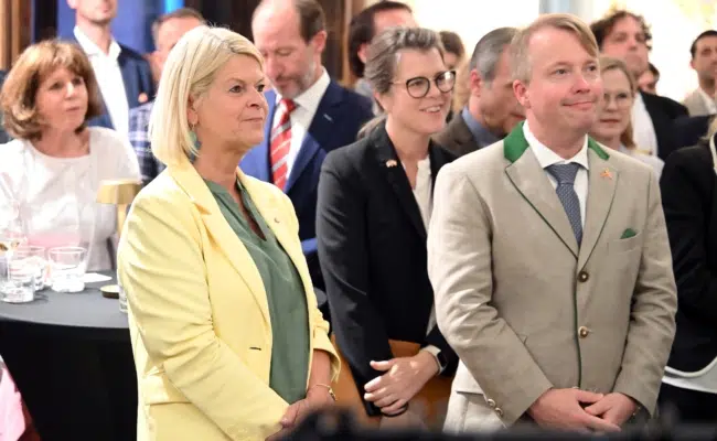 US-Botschafter Art Fisher steht neben Klaudia Tanner und hört dem Panel zu. Im Hintergrund sind Gäste und Medienvertreter zu sehen.