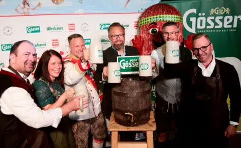 ertreter der Wiener Kaiser Wiesn und ihrer Partner stoßen vor einer Gösser Werbewand mit Bierkrügen an