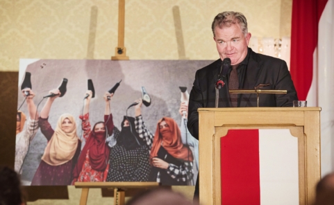 Cornelius Obonya spricht am Rednerpult. Links neben ihm zeigt Silvia Alessis Siegerfoto afghanische Frauen mit erhobenen Haartrocknern.