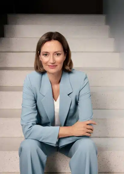 Bettina Schausten in einem hellblauen Hosenanzug auf einer Treppe