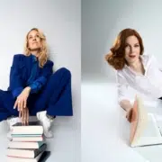 Lilian Klebow im blauen Anzug hinter einem Bücherstapel und Teresa Vogl in weißer Bluse mit einem aufgeschlagenen Buch.