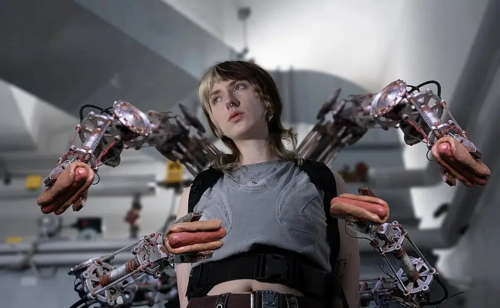 Eine junge Person trägt eine Apparatur mit vier mechanischen Armen, die jeweils einen Hotdog halten.
