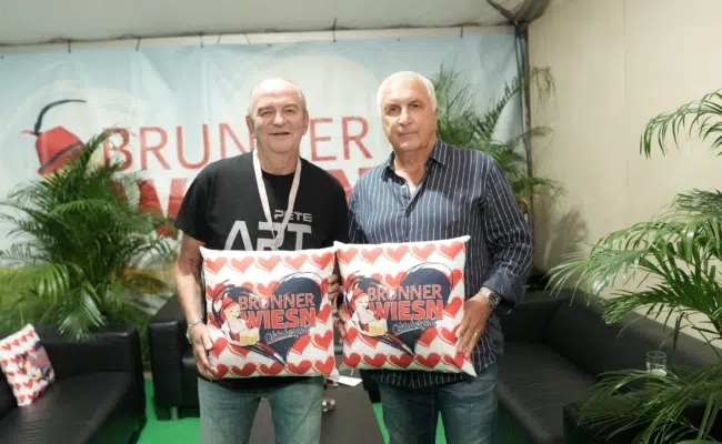 Herbert Prohaska und Hans Krankl präsentieren zwei Dekokissen mit dem Logo der Brunner Wiesn.