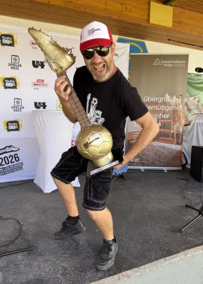Roman Gregory hält die goldene Trophäe mit Fußball, Gitarrenhals und Fußballschuh in die Kamera.
