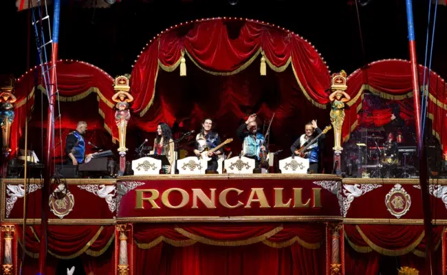 Musiker und eine Sängerin auf der rot-goldenen Orchesterbühne von Roncalli, mit Keyboard, Gitarre, Geige, Bass und Schlagzeug.