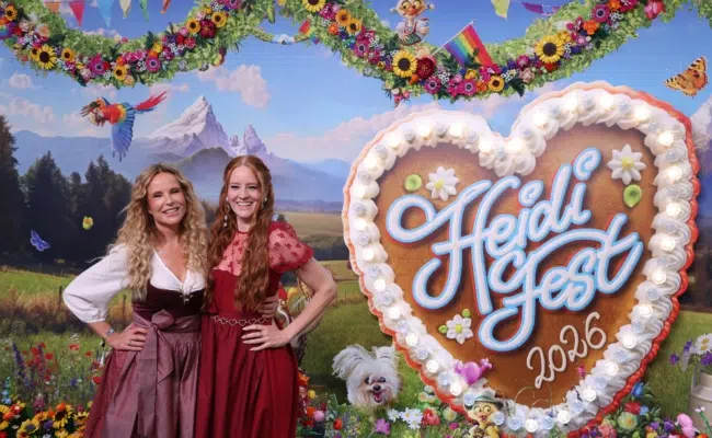 Katja Burkard und Barbara Meier posieren in Dirndln neben einem großen „HeidiFest 2026“-Lebkuchenherz.
