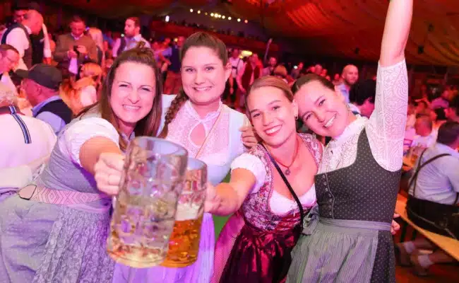 Vier Frauen in Dirndln halten Bierkrüge in die Höhe und feiern gemeinsam im Festzelt der Brunner Wiesn.