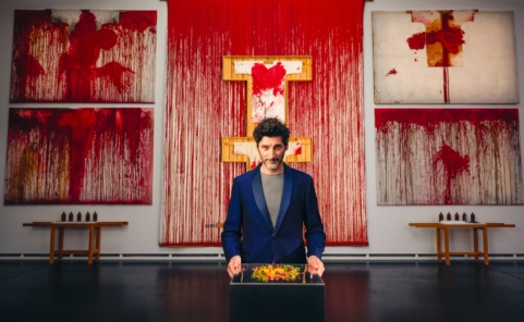 Paul Ivić präsentiert vor blutroten Werken von Hermann Nitsch ein vegetarisches Gericht.
