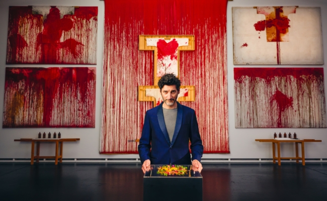 Paul Ivić präsentiert vor blutroten Werken von Hermann Nitsch ein vegetarisches Gericht.