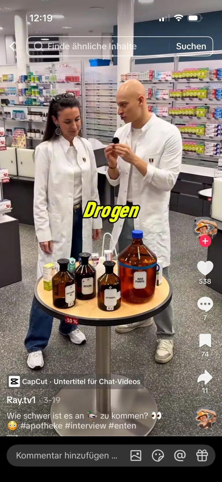 Ray und eine Apothekerin stehen im weißen Kittel vor einem Tisch mit Flaschen und Packungen.