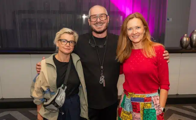 Angelika Molk, Wolfgang Reichl und Maja Kölich Angelika Molk, Wolfgang Reichl und Maja Kölich stehen gemeinsam vor einem violett beleuchteten Hintergrund.