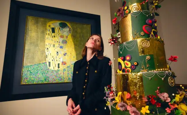 Sophia Stolz steht mit ihrer mehrstöckigen Tortenkreation vor Gustav Klimts „Der Kuss“.