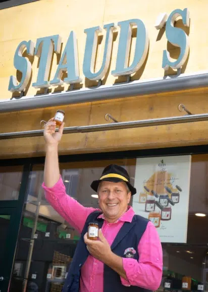 Stefan Schauer hält zwei Gläser Roncalli-Marillenmarmelade vor dem STAUD’S-Pavillon am Wiener Brunnenmarkt.