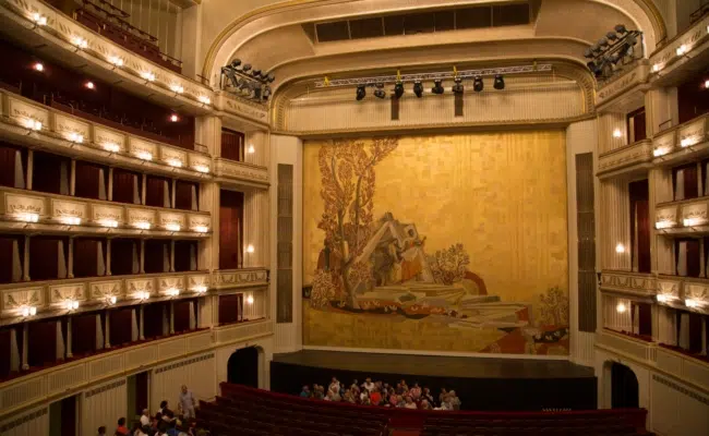 Goldfarbener Eiserner Vorhang mit Eisenmengers Darstellung von Orpheus und Eurydike im goldenen und roten Zuschauerraum der Wiener Staatsoper.