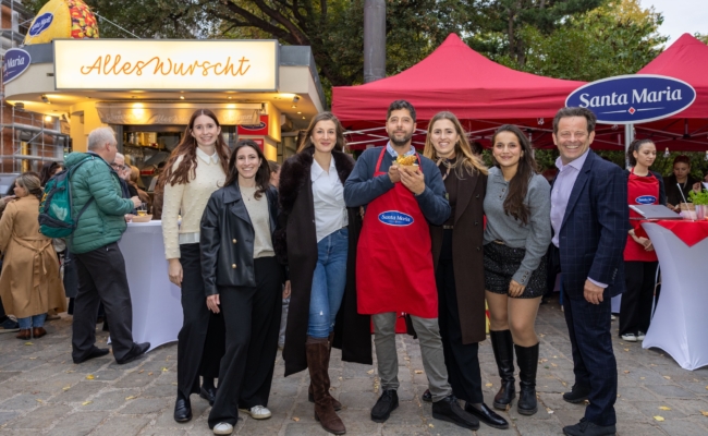 Gruppenfoto vor „Alles Wurscht“ mit Sebastian Neuschler in roter Schürze in der Mitte, Alexander Zoubek rechts und Brigitta Wölfer.