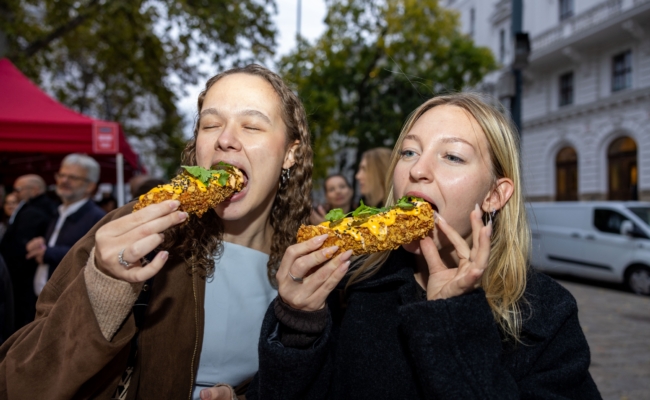 Zwei Besucherinnen beißen in ihre mit Saucen und Kräutern belegten Nacho Dogs.