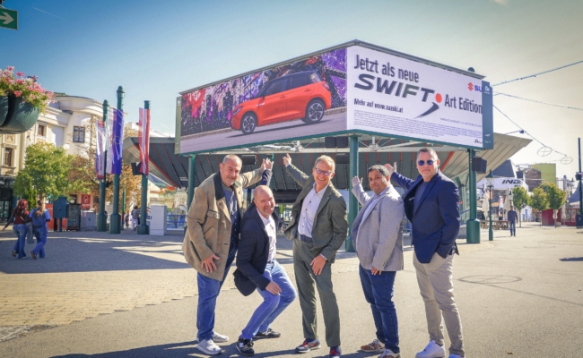 Fünf Männer vor der LED-Werbefläche mit einer Suzuki-Swift-Kampagne am Wiener Riesenradplatz.