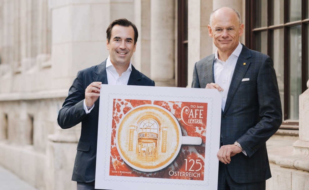 Martin Winkler und Walter Oblin halten eine vergrößerte Darstellung der Jubiläumsbriefmarke vor dem Café Central.