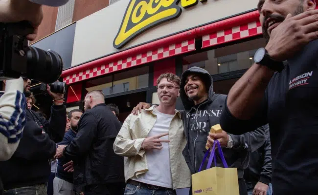 Besucherinnen und Besucher vor dem Eingang von Loco Chicken in Wien, im Vordergrund wird ein Smartphone hochgehalten.