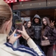 Luciano posiert mit zwei Fans am Eingang von Loco Chicken, eine Person im Vordergrund fotografiert mit dem Smartphone.