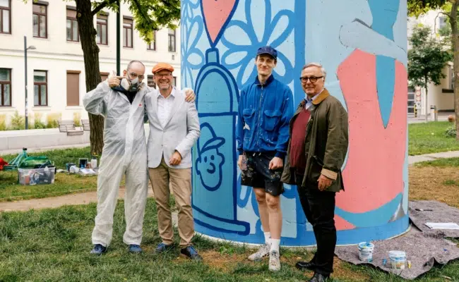 Vier Projektbeteiligte vor dem bunt gestalteten Lüftungsturm „Füreinander“ im Helga-Pollak-Kinsky-Park.
